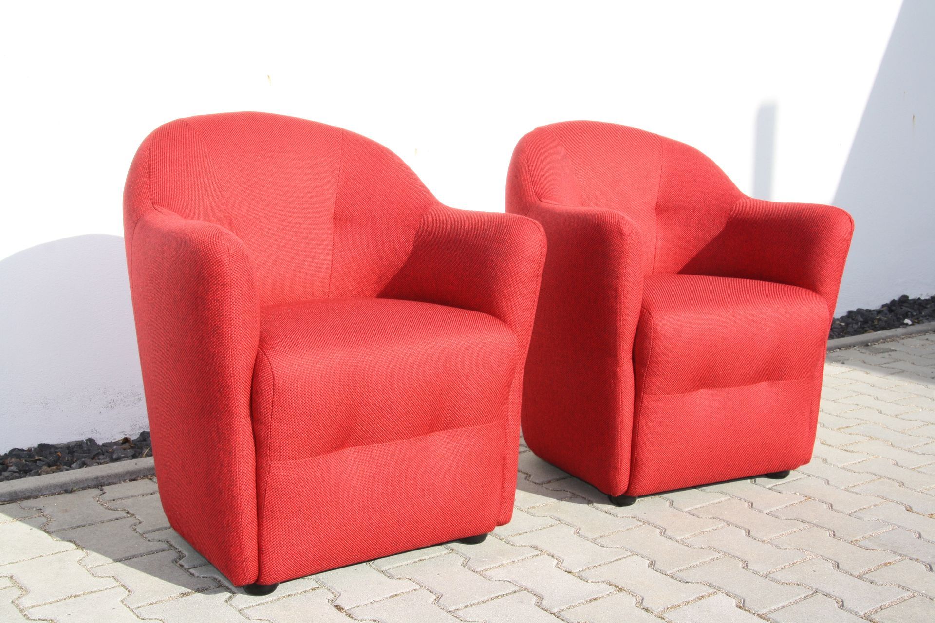 Zwei rote Stühle stehen nebeneinander auf einem gemauerten Bürgersteig