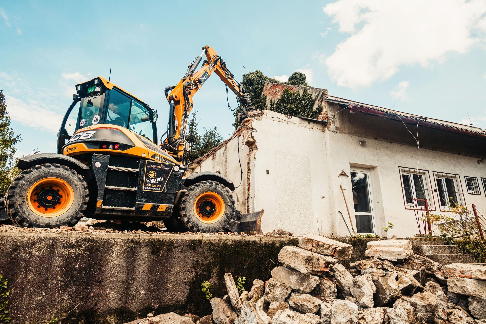 Una excavadora demuele una casa blanca, con escombros en primer plano.
