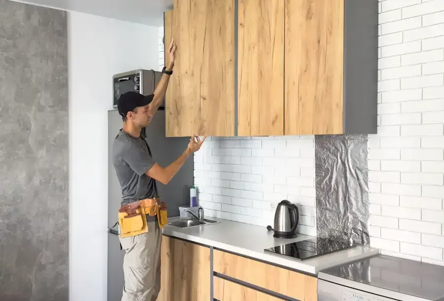 Persona instalando un mueble de cocina de madera encima de una encimera y un fregadero.