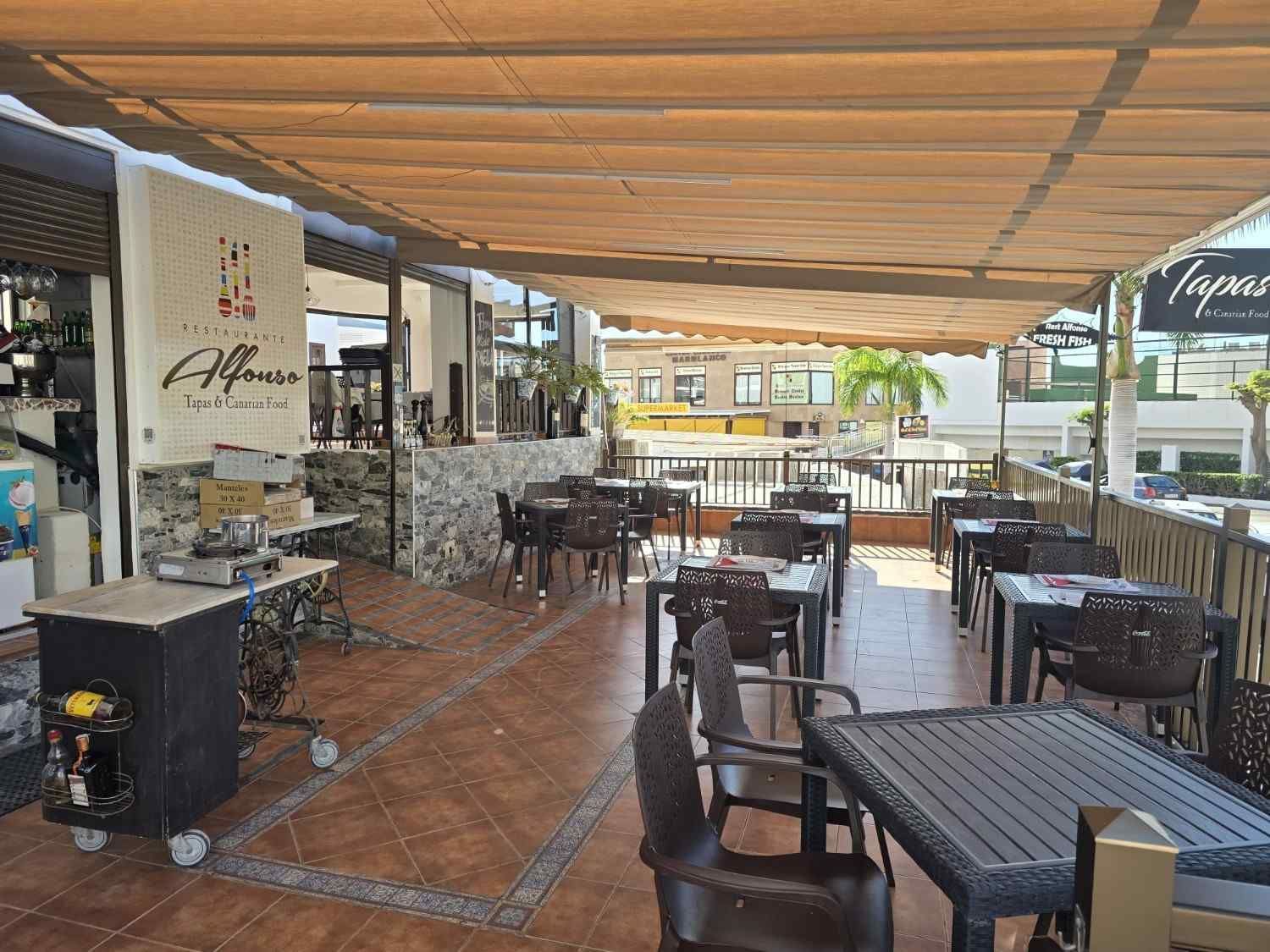 Restaurante al aire libre con mesas y sillas dispuestas bajo un dosel, día soleado.