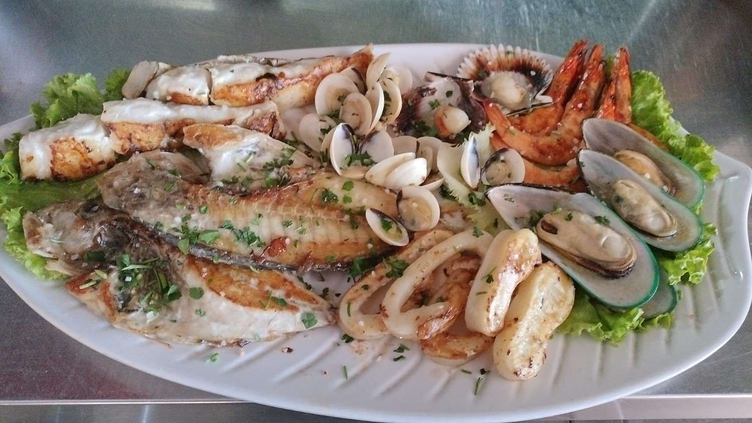 Plato de mariscos: pescado a la parrilla, camarones, mejillones, almejas, calamares y vieiras en un plato.