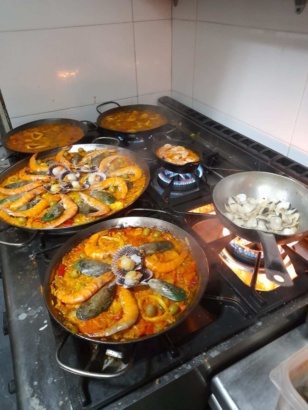 Varias paelleras con mariscos cocinándose en una estufa en una cocina.
