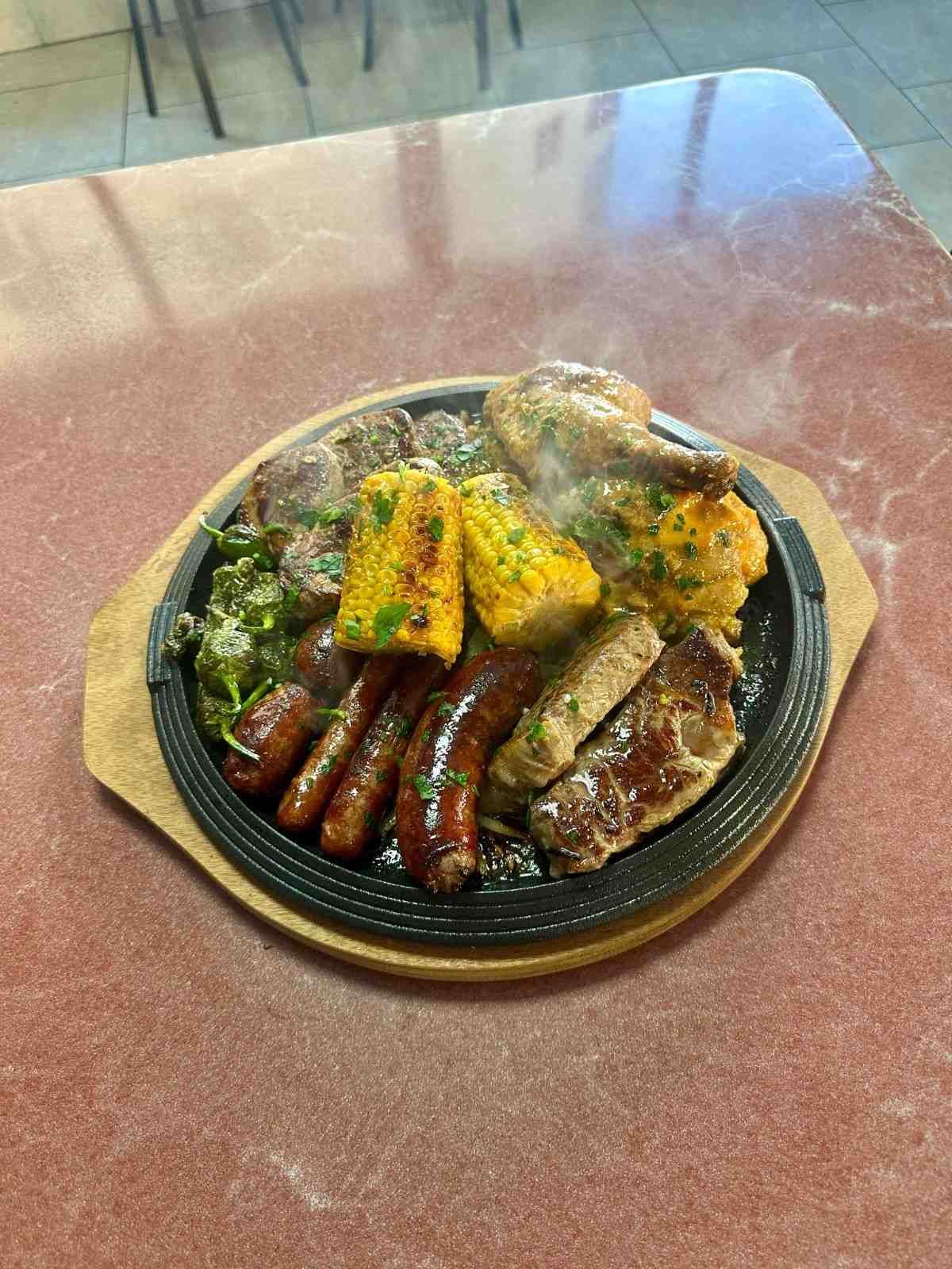 Carne y verduras a la parrilla en una fuente chisporroteante: salchichas, maíz, pollo y filete.