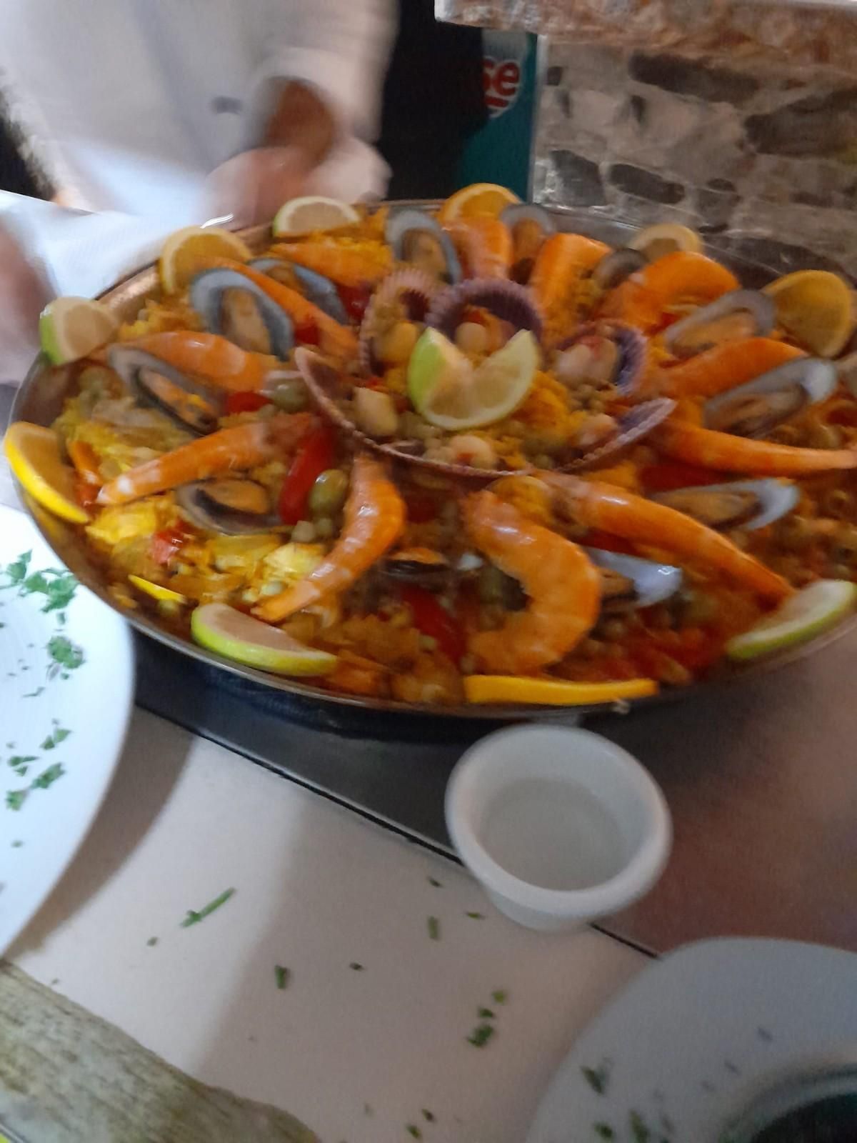 Paella con camarones, mejillones y almejas, adornada con rodajas de limón, en una sartén grande sobre una mesa.