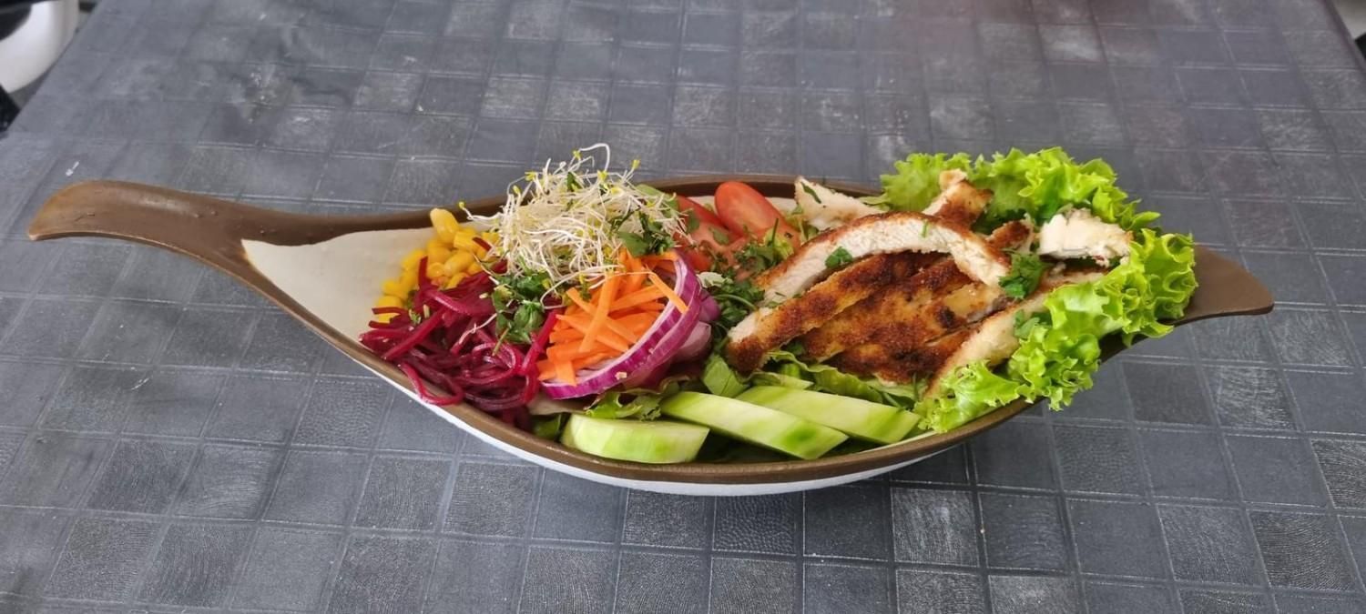 Una ensalada con pollo en un tazón marrón sobre una superficie gris. Verduras: lechuga, pepino, zanahoria y coles.