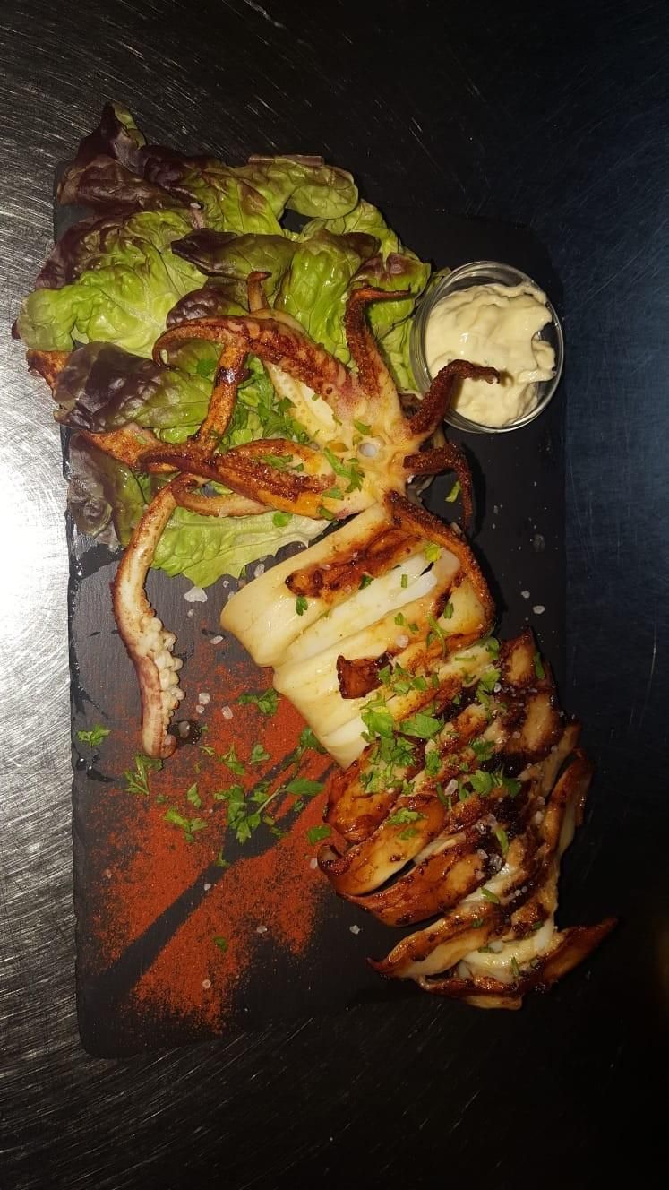 Calamares a la plancha con ensalada y salsa, servidos en plato rectangular negro.