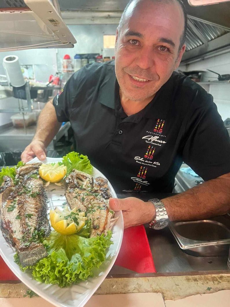 Chef sosteniendo un plato de pescado a la parrilla adornado con limón y perejil.