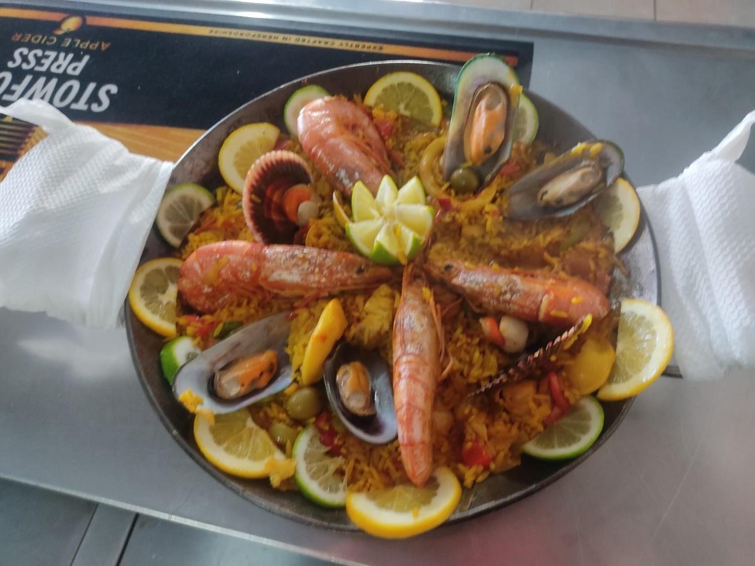 Paella de marisco en sartén grande, adornada con rodajas de limón y mariscos.