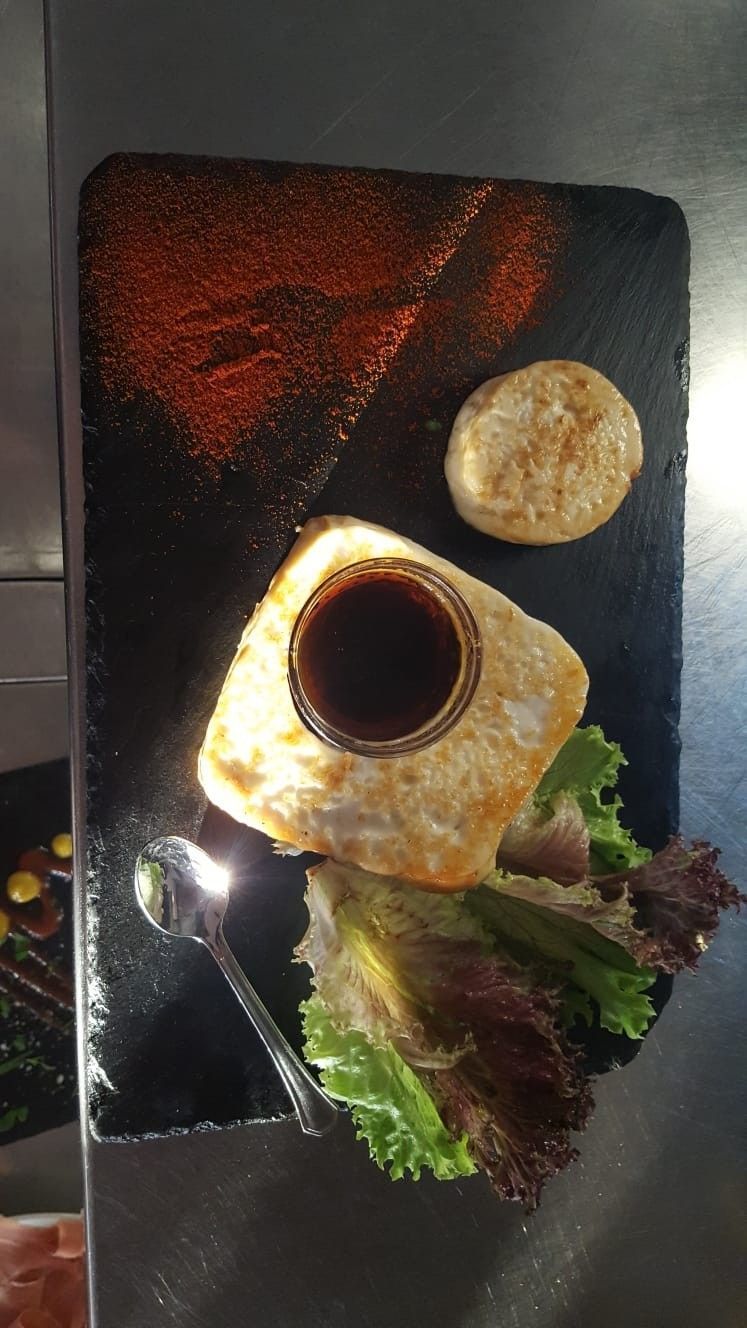 Huevo frito con salsa, guarnición y un pequeño acompañamiento sobre una pizarra negra.
