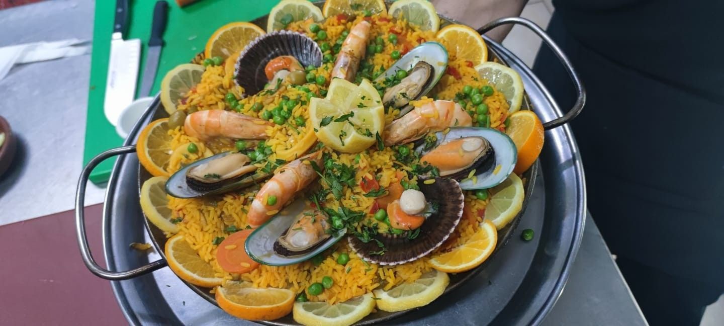 Paella con mejillones, camarones, vieiras y rodajas de limón en sartén metálica.
