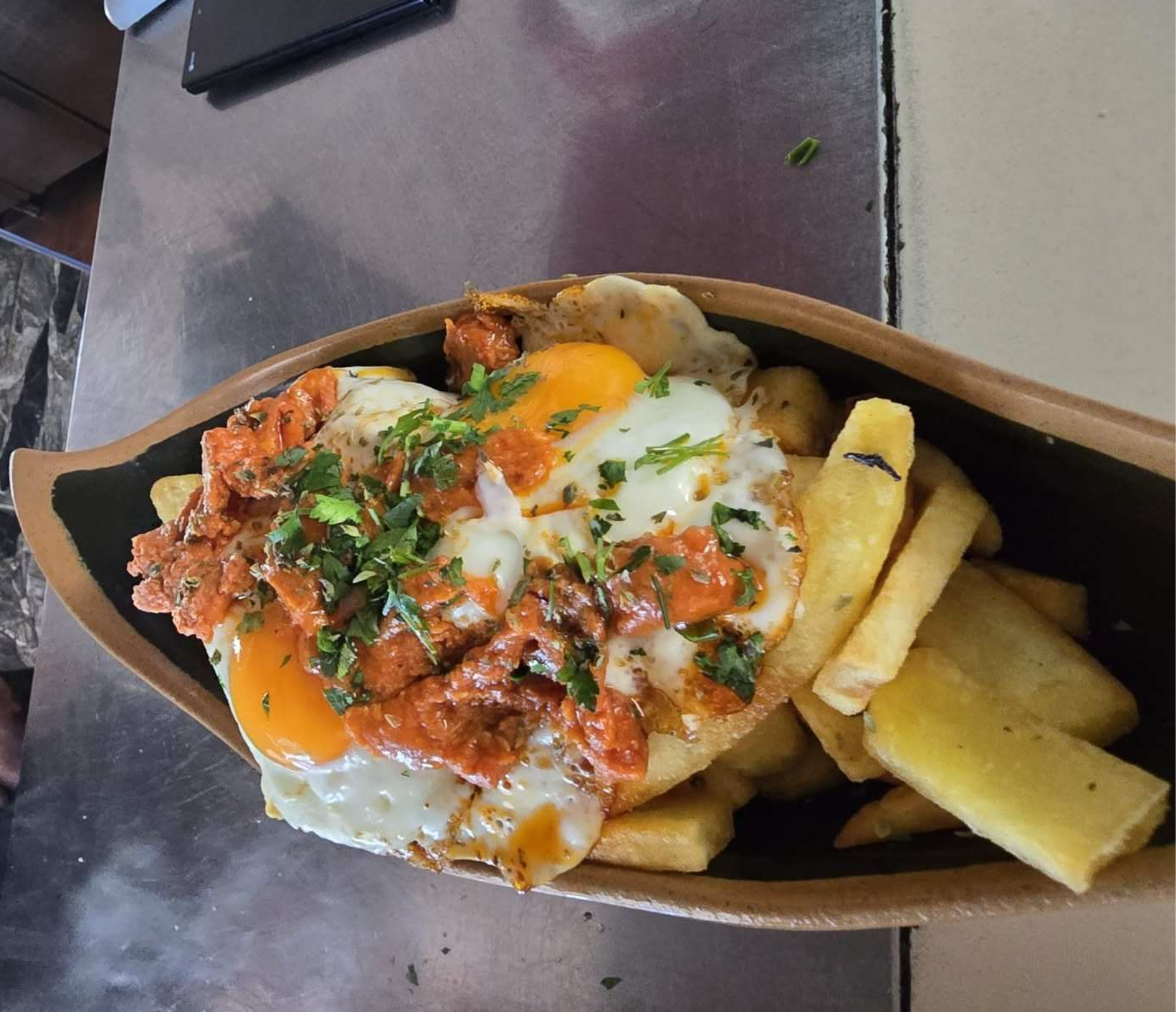 Huevos fritos con chorizo ​​y perejil sobre patatas fritas, servidos en cuenco de madera.