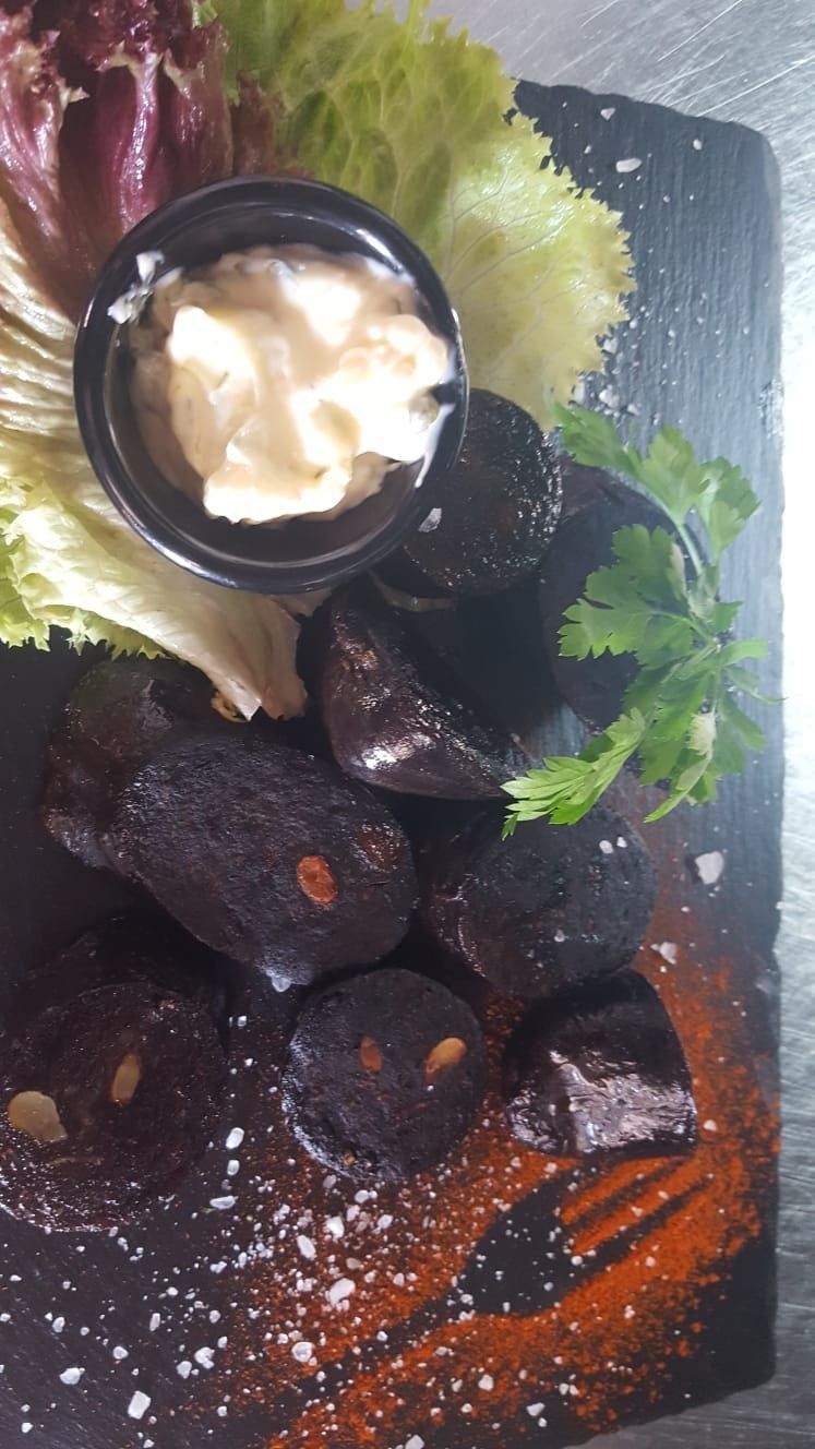 Comida ennegrecida con salsa blanca, lechuga y condimentos en una bandeja de pizarra.