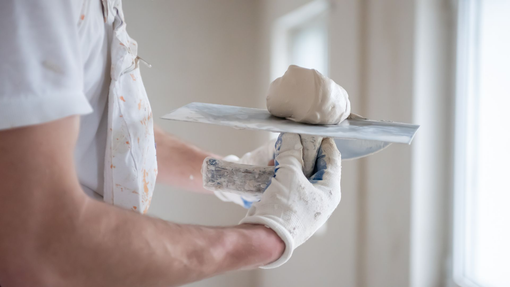 Personne gantée tenant une truelle à plâtre avec du plâtre frais.
