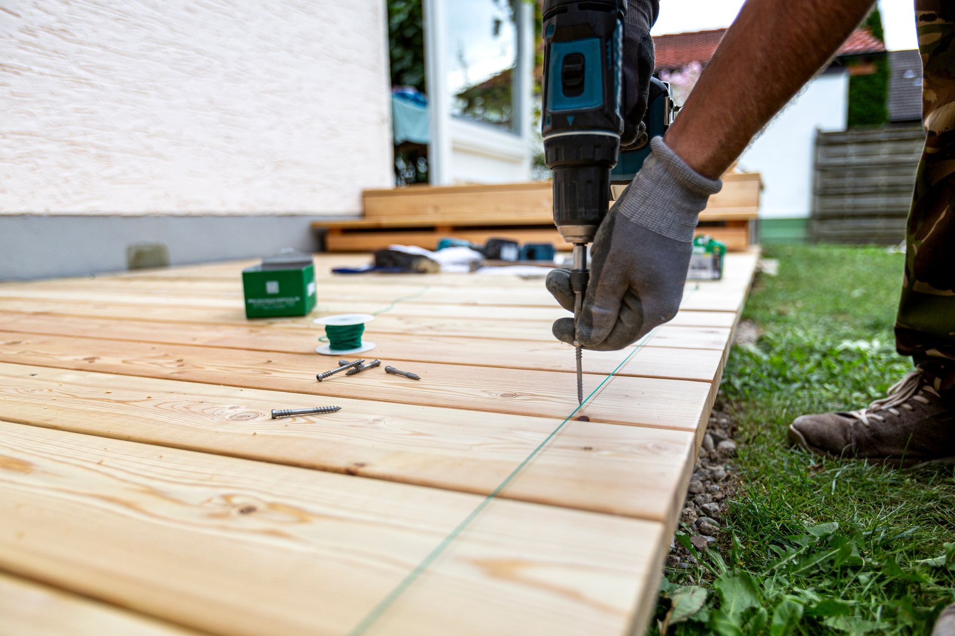 Une personne utilise une perceuse pour fixer des planches d'une terrasse en bois à l'extérieur.