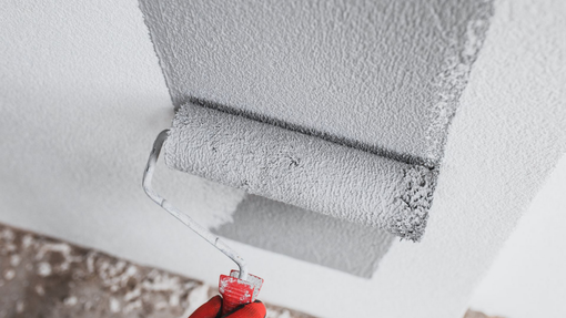 Main gantée de rouge peignant un mur blanc au rouleau fixé à une perche.