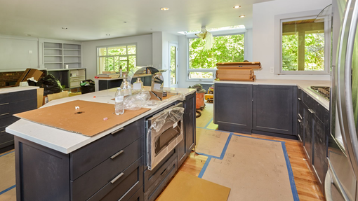 Cuisine moderne en cours de rénovation avec placards foncés, îlot central et sol masqué par du ruban adhésif.
