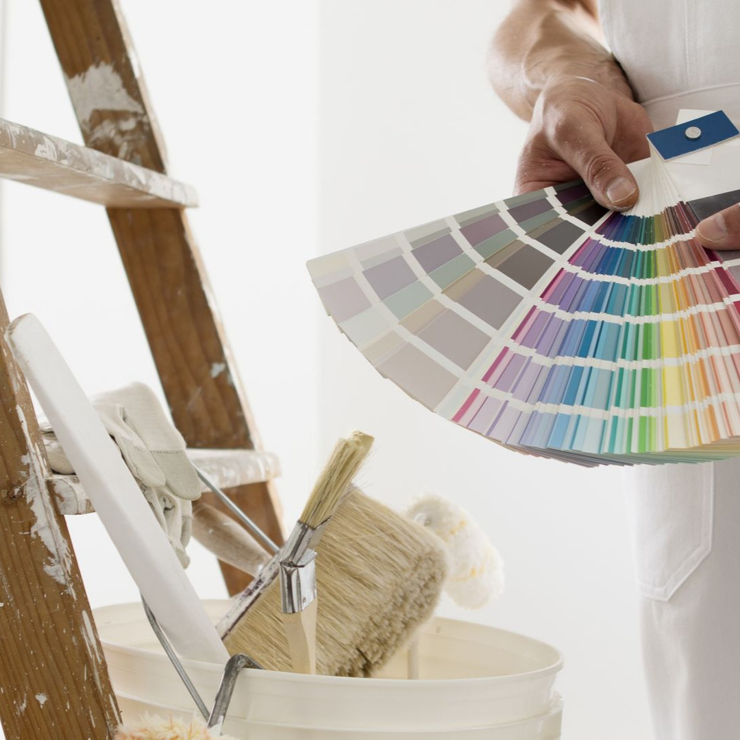 Une peintre tient des échantillons de peinture, à côté d'une échelle et d'un pot de peinture.