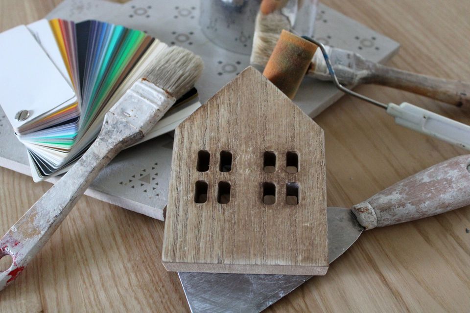 Maquette d'une maison en bois posée sur une table de travail, avec du carrelage, des pinceaux et un nuancier.