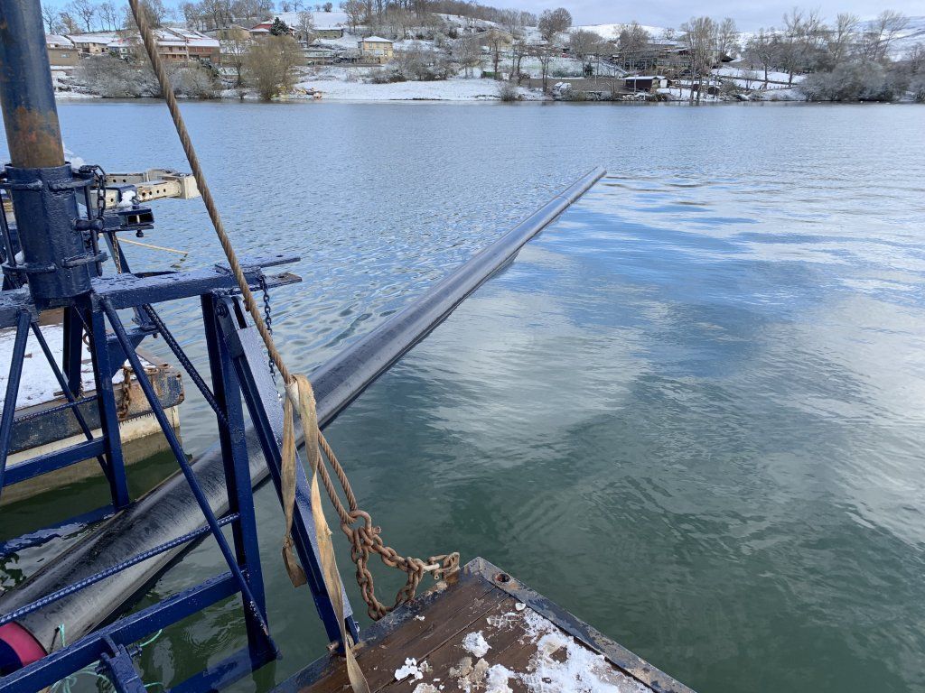 Un barco azul en el agua, con una larga pala sumergida. Al fondo, la orilla nevada.