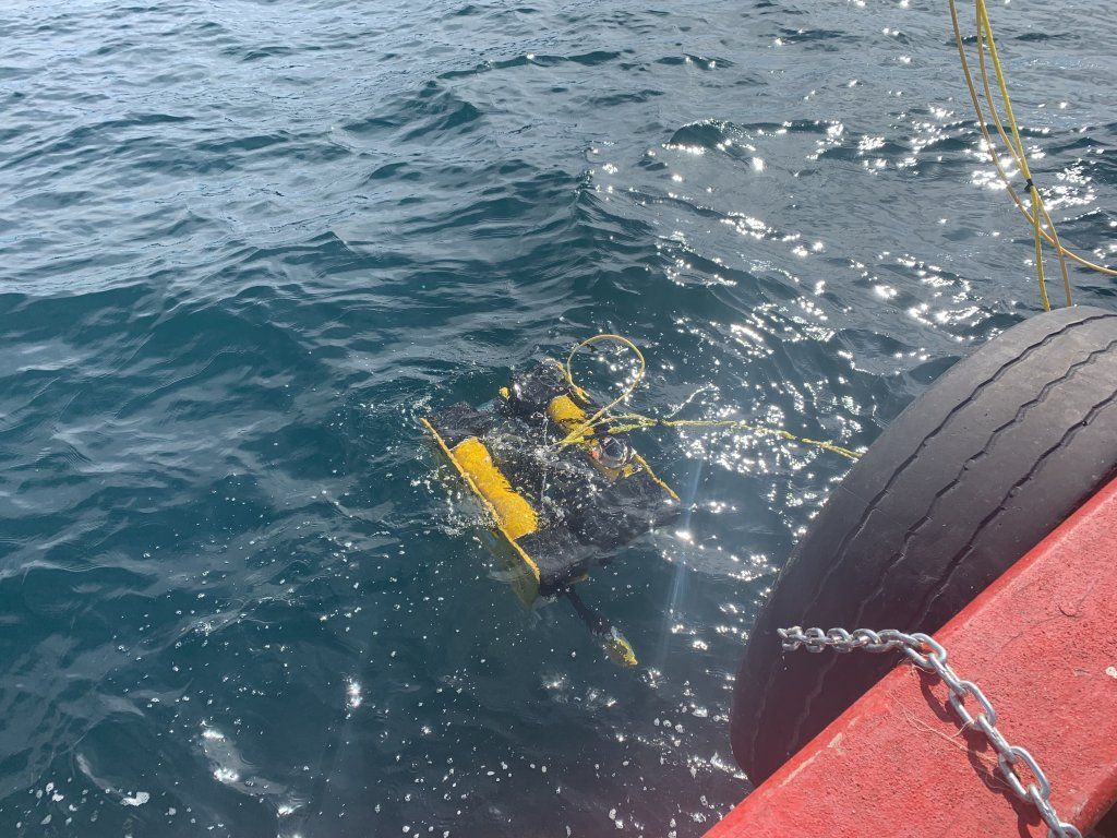 Trampa para cangrejos en agua de mar junto a la llanta y el costado rojo de un bote; cadena adjunta.