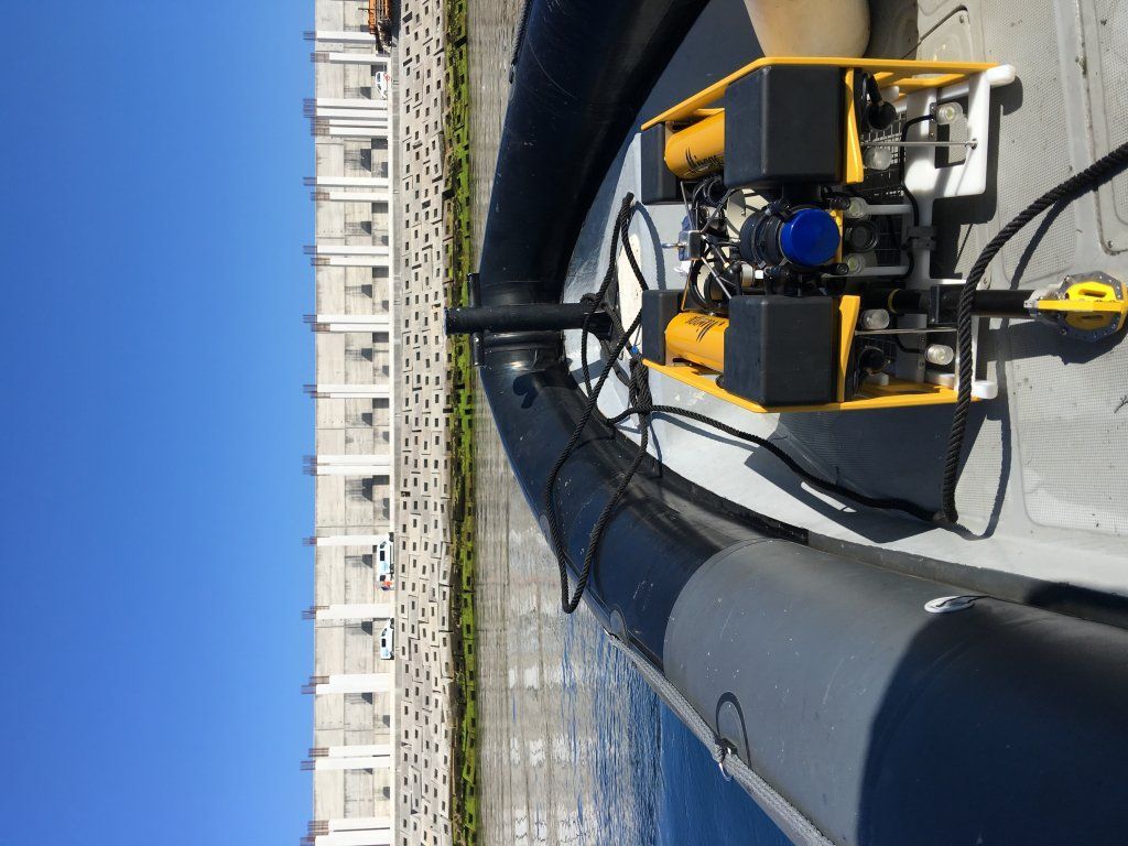 Un bote inflable negro con un motor amarillo, sobre un fondo de edificios de concreto y un cielo azul.
