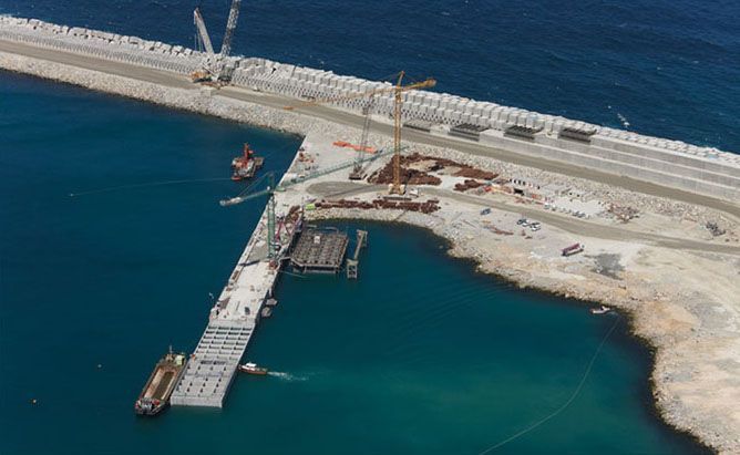 Obras en un puerto. Grúas, estructuras de hormigón y barcos en aguas turquesas.
