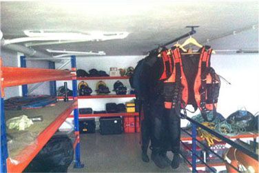 Trastero con estanterías y equipo de rescate colgado. Chalecos, cascos y equipo naranja y negro.