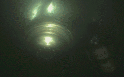 Objeto cilíndrico brillante con una fuente de luz central brillante, rodeado de formas oscuras y borrosas.