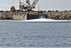 Grúa bajando una estructura al océano, creando un gran chapoteo. Al fondo, una costa rocosa.