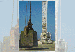 Grúa levantando un gran bloque de hormigón en un sitio de construcción contra un cielo azul.