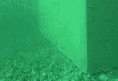 Vista teñida de verde de un muro de hormigón y suelo de grava.