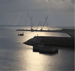 Un mar nublado y reflectante con varias grúas en un muelle rocoso.