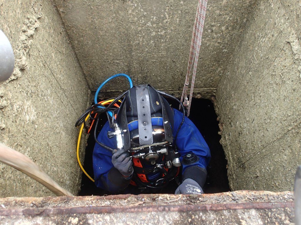 Buzo con traje azul, descendiendo a un espacio oscuro y rectangular desde arriba.