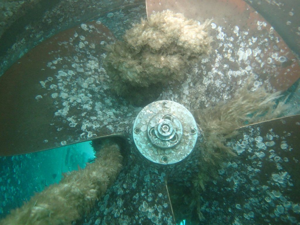 Hélice de barco cubierta de crecimiento marino bajo el agua.