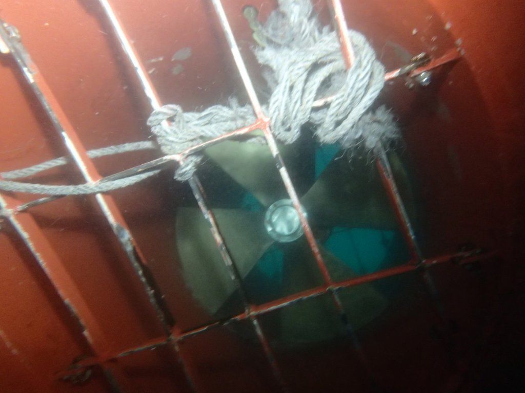 Una hélice dentro de una jaula metálica, sujeta con cuerda. La hélice tiene palas verdes.