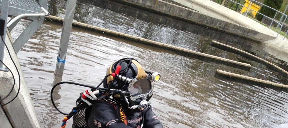 Un buzo con equipo completo examina un sistema de agua con tuberías y estructuras de hormigón.