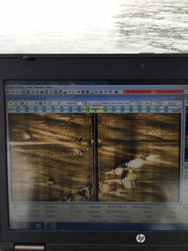 Pantalla de sonar que muestra el terreno submarino, una línea vertical central y objetos dispersos en un cuerpo de agua.