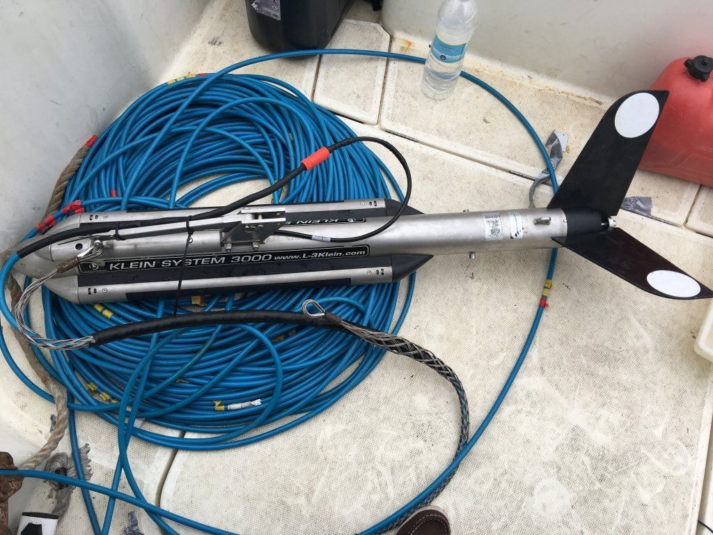 Un dispositivo planeador submarino con un cable azul enrollado en la cubierta de un barco.