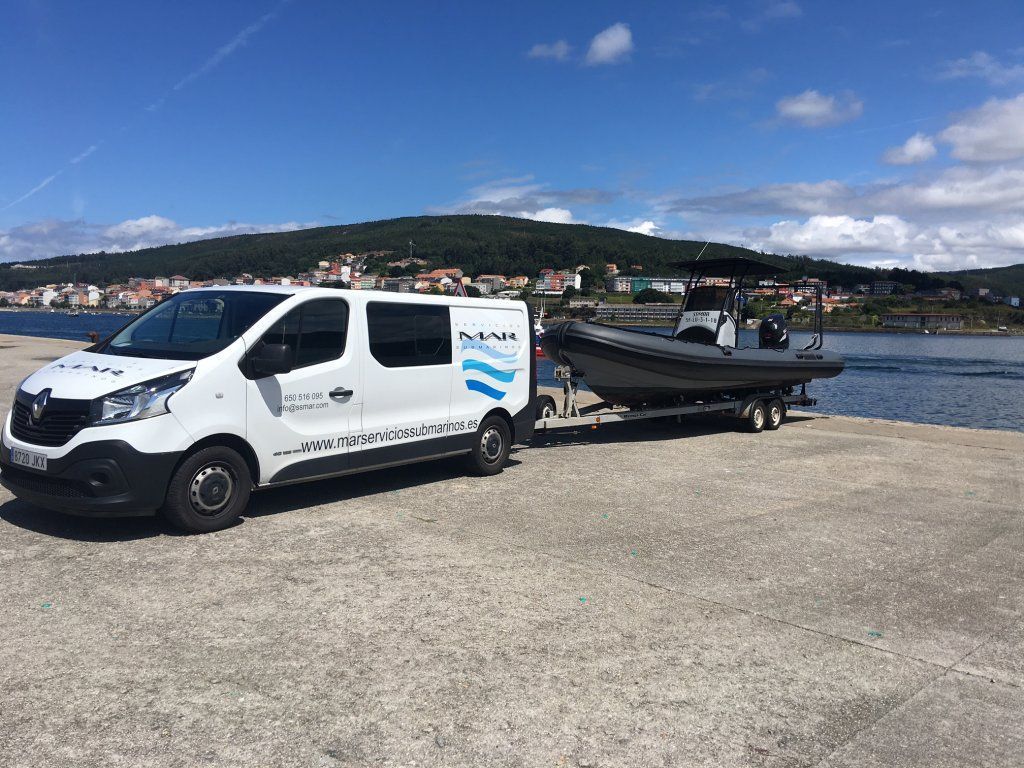 Una camioneta blanca remolca un barco negro en un remolque junto a un puerto en un día soleado.