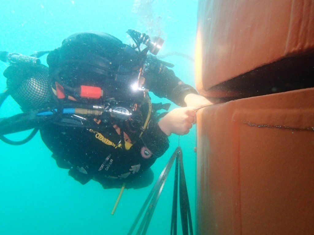 Buceador tocando una estructura submarina naranja. Agua turquesa lo rodea.