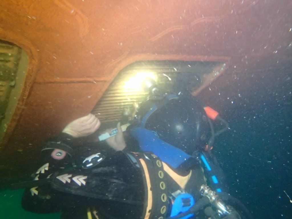 Buceadores dentro de una estructura sumergida, iluminada por una luz brillante.