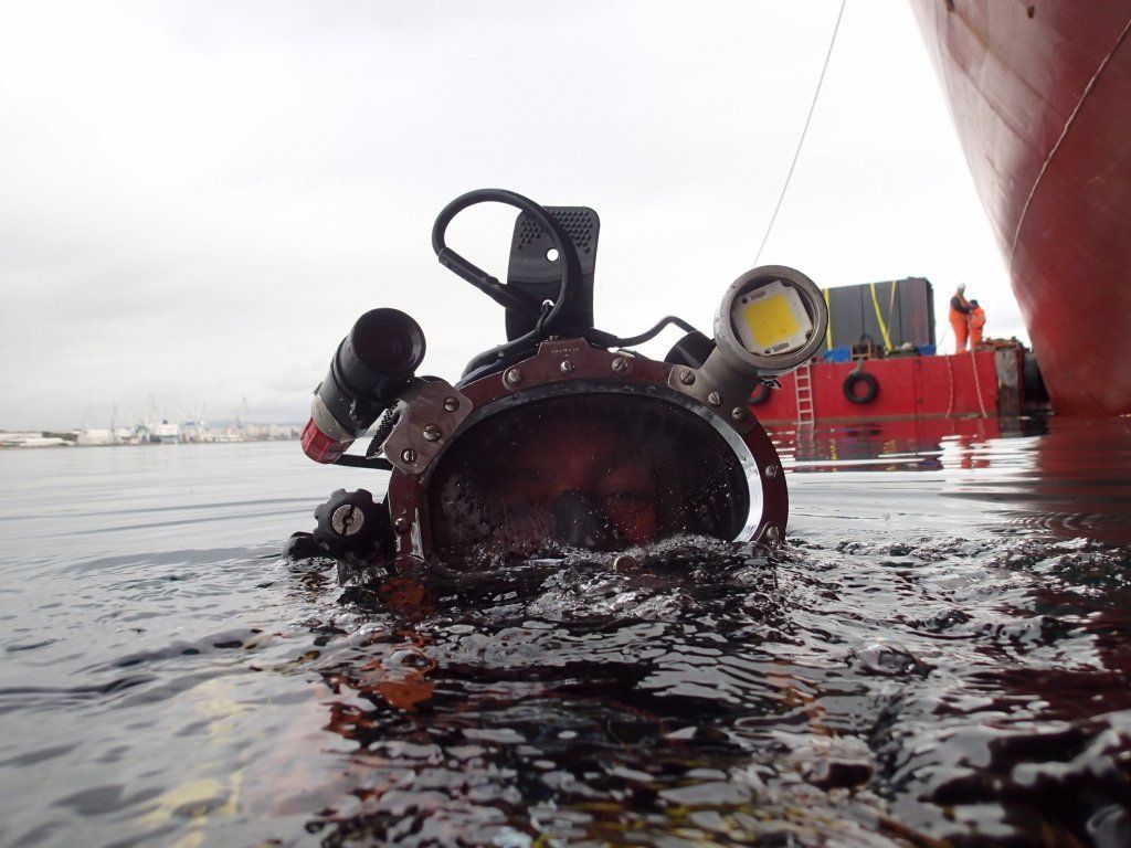 Casco de buceo en el agua, con luces incorporadas, cerca de un barco, en un puerto.