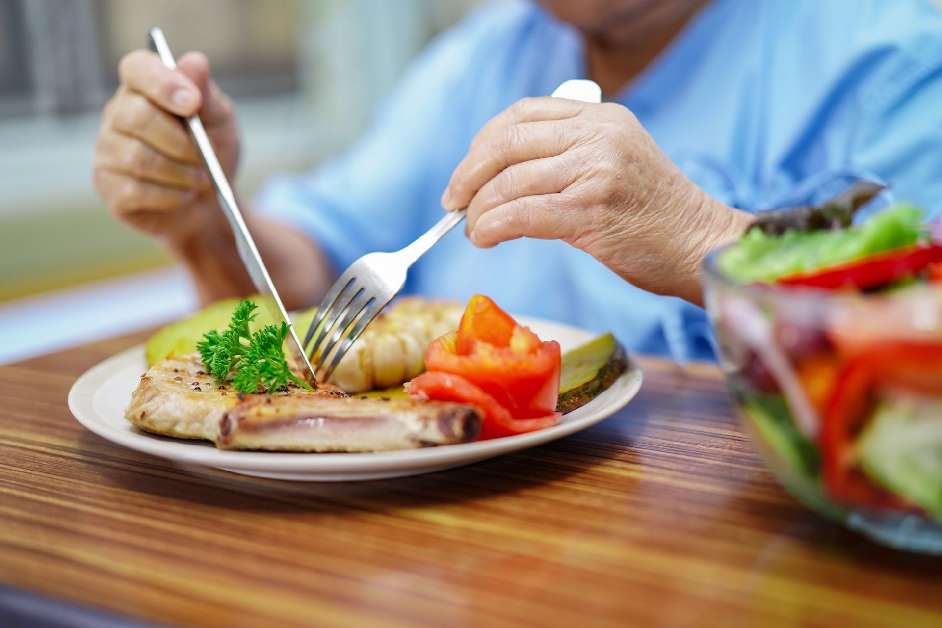 Des mains utilisent une fourchette et un couteau pour couper des aliments dans une assiette de légumes à une table à manger