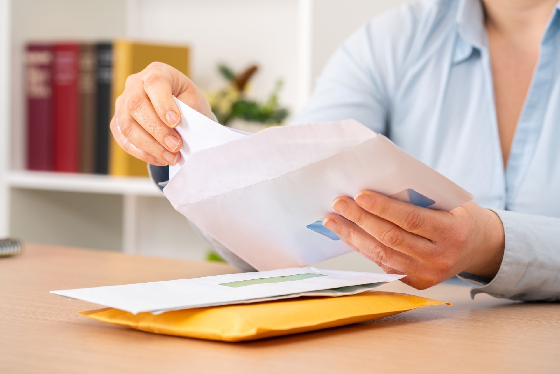 Une personne ouvre du courrier dans une enveloppe blanche posée sur un bureau