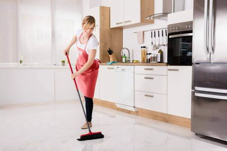 Femme avec tablier passant le balai dans une cuisine moderne