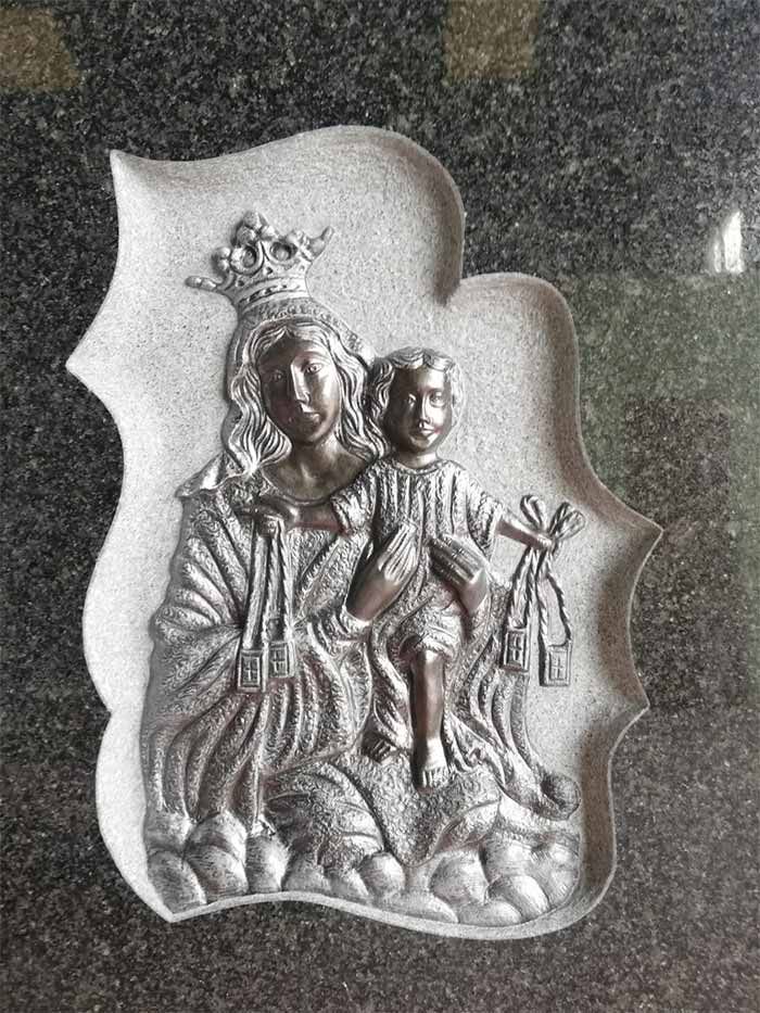 Una estatua de una mujer sosteniendo al Niño Jesús sobre una superficie negra.
