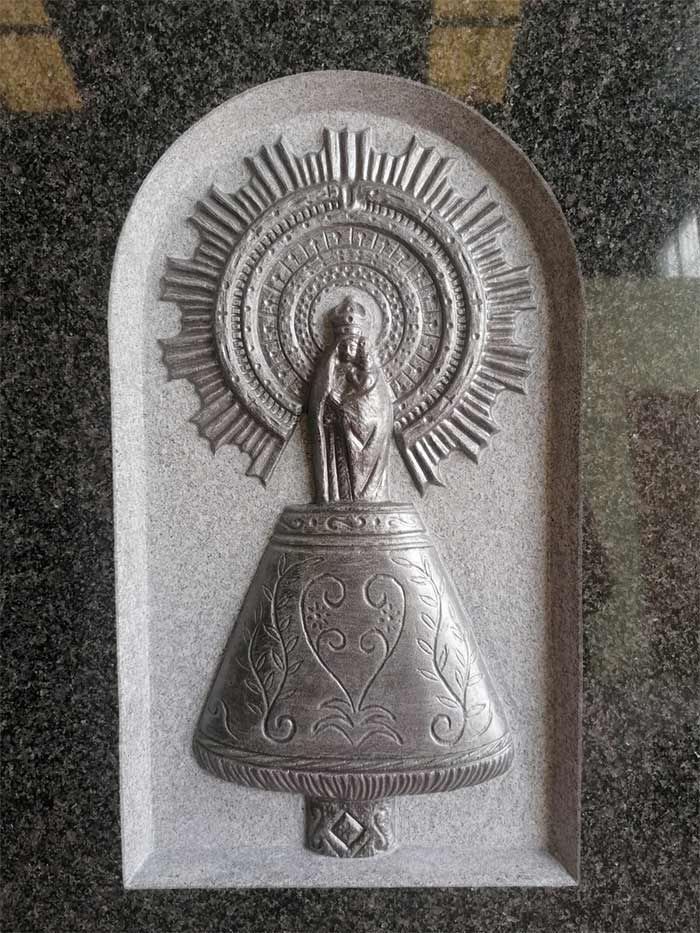 Una estatua de una mujer sosteniendo un bebé en una campana en una pared.