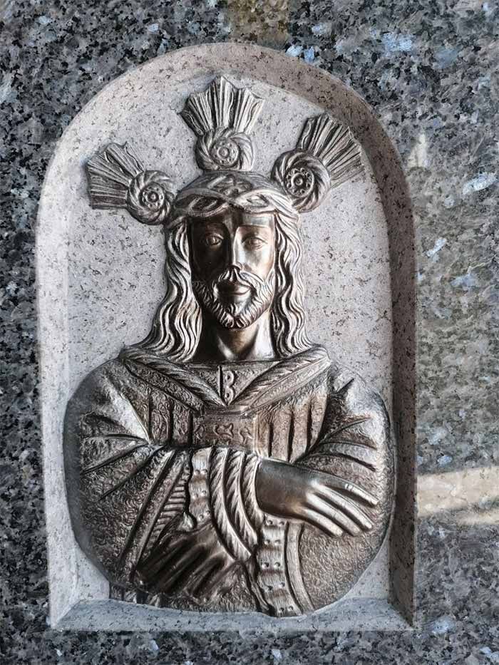 Una estatua de Jesús con una corona de espinas en la cabeza está sobre una pared de granito.