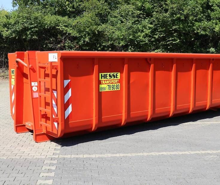 Ein leuchtend orangefarbener Bauschuttcontainer auf einer gepflasterten Straße neben Grünflächen