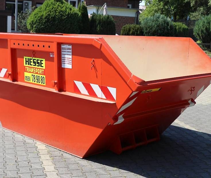 Ein orangefarbener Bauschuttcontainer auf einer asphaltierten Straße